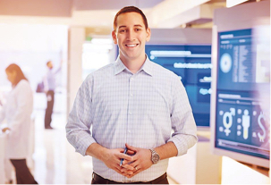 A smiling young man standing in front of large screens displaying Express Scripts Canadas data insights work