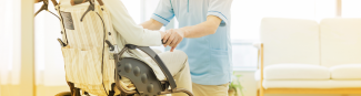 Gros plan d'un jeune professionnel de la santé vêtu d’un sarrau bleu qui est agenouillé devant un patient en fauteuil roulant.