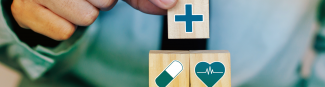 Person placing wooden block with cross icon on top of two other wooden blocks with a pill and heart symbol on each
